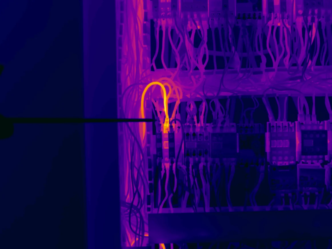 Imagem térmica de um quadro elétrico com conexões aquecidas em destaque