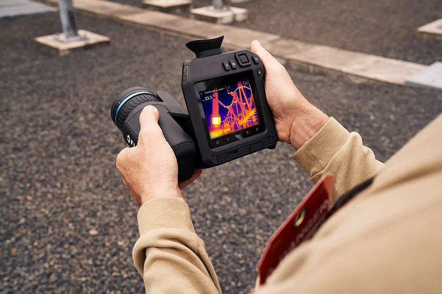 Termografista segurando câmera térmica FLIR durante inspeção em subestação ao ar livre